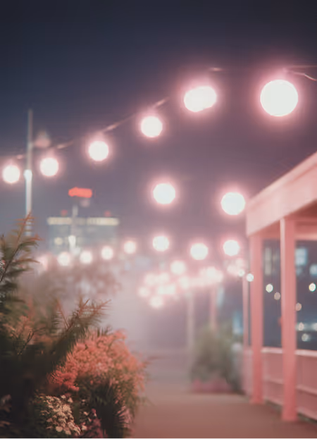 String lights glowing above a walkway with plants and a white railing at night.